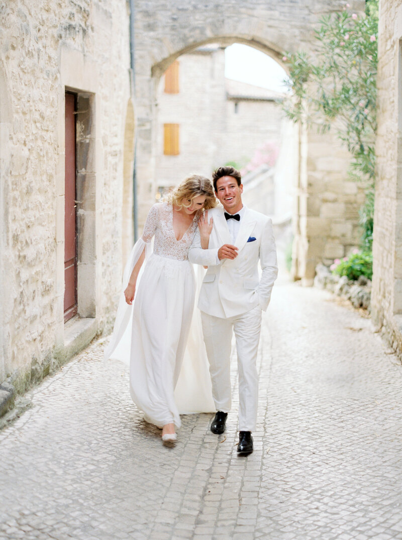 Bride and groom walk arm in arm down cobblestone street in France
