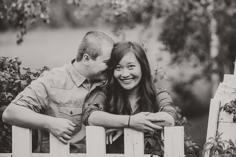 engaged couple leans on picket fence