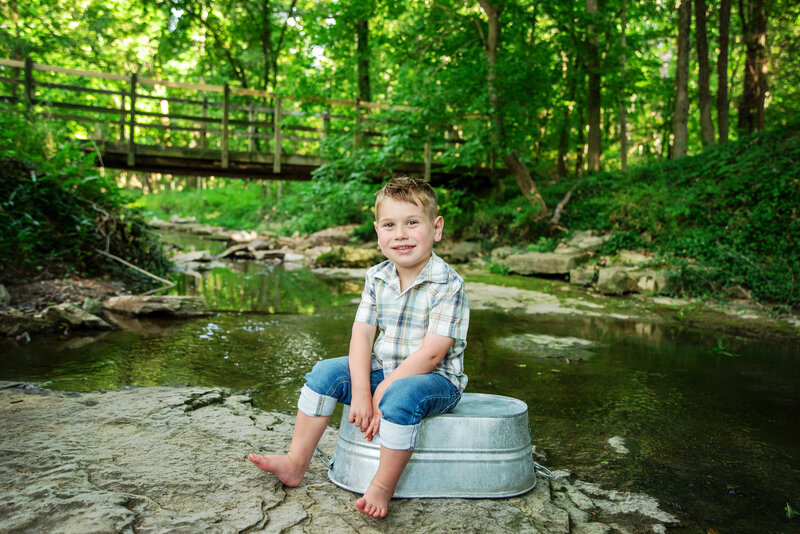 st-louis-mini-session-photographer-creek-mini-session-boy-in-front-of-bridge-and-water-sitting-on-bucket