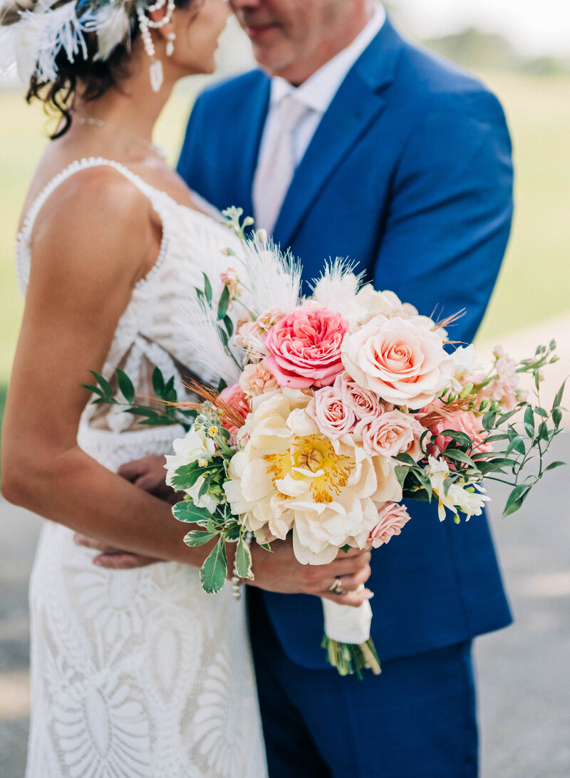 Bride and groom hugging with a bouquet of pink whimsical flowers