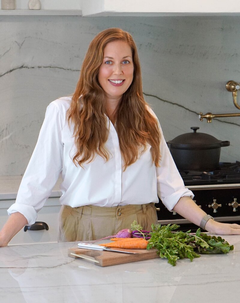 Owner and designer Nikki Parrish standing in Mordecai gourmet kitchen cutting vegetables on marble countertop.