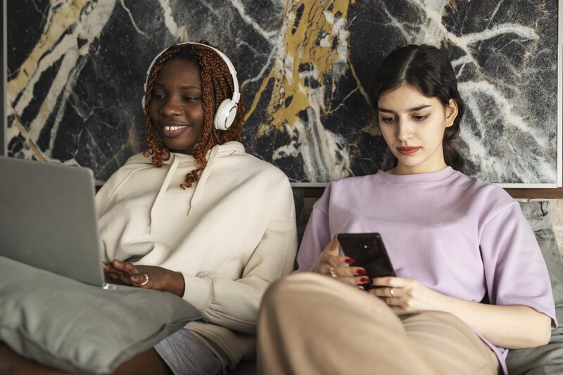 woman wearing headphones next to woman on iphone