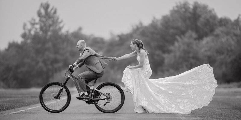 Award-winning black and white photo of a couple joyfully riding a bike, showcasing timeless wedding photography.