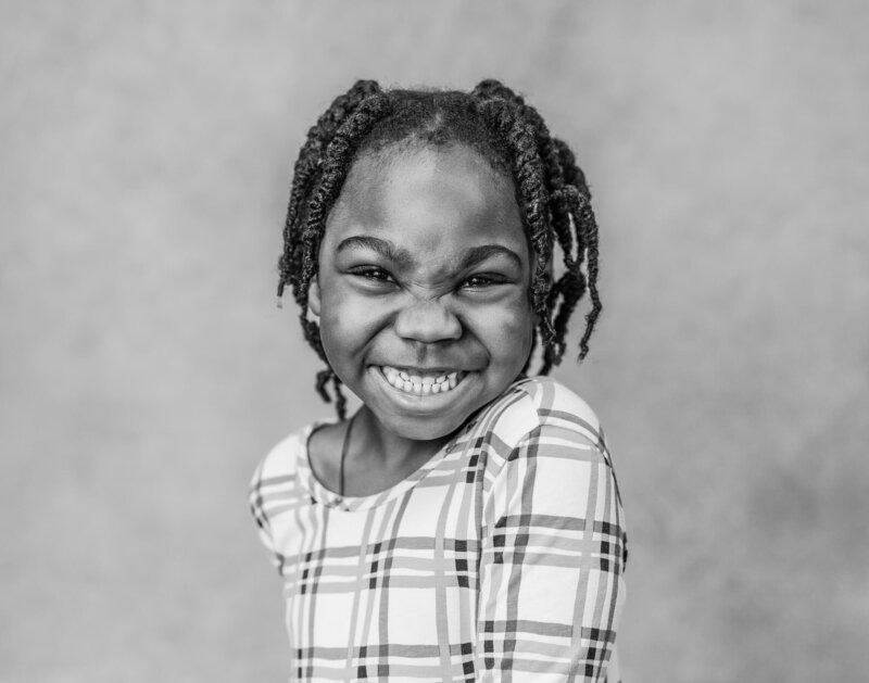 A close up short of a child smiling, their one shoulder forward.