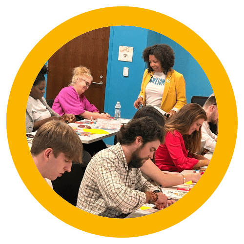 Photo of Michelle McKown-Campbell smiling while workshop participants are working on an interactive confidence building activity with construction paper