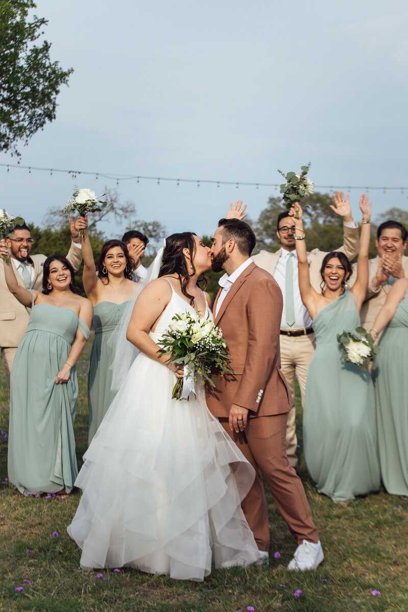Bride and groom share a kiss in front of their wedding party for San Antonio wedding photographer