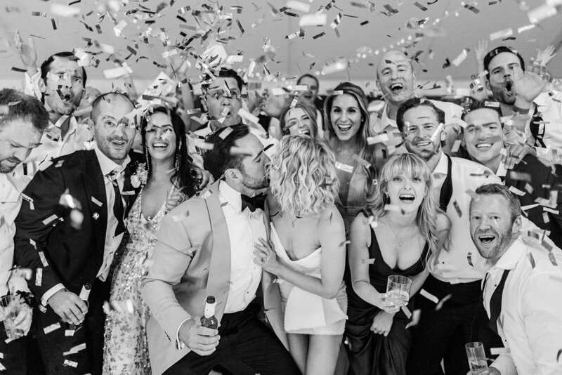 A joyous black and white photograph of a wedding party celebrating, with guests laughing and confetti flying through the air, showcasing expert party planning.