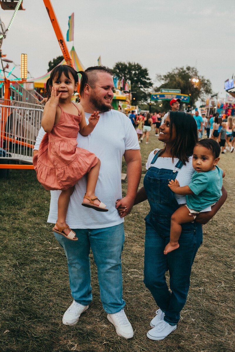 Owner Channa Brouk holding hands with her husband while holding kids during the Washington Missouri Town & County Fair | About Us | Evalyn & Co.