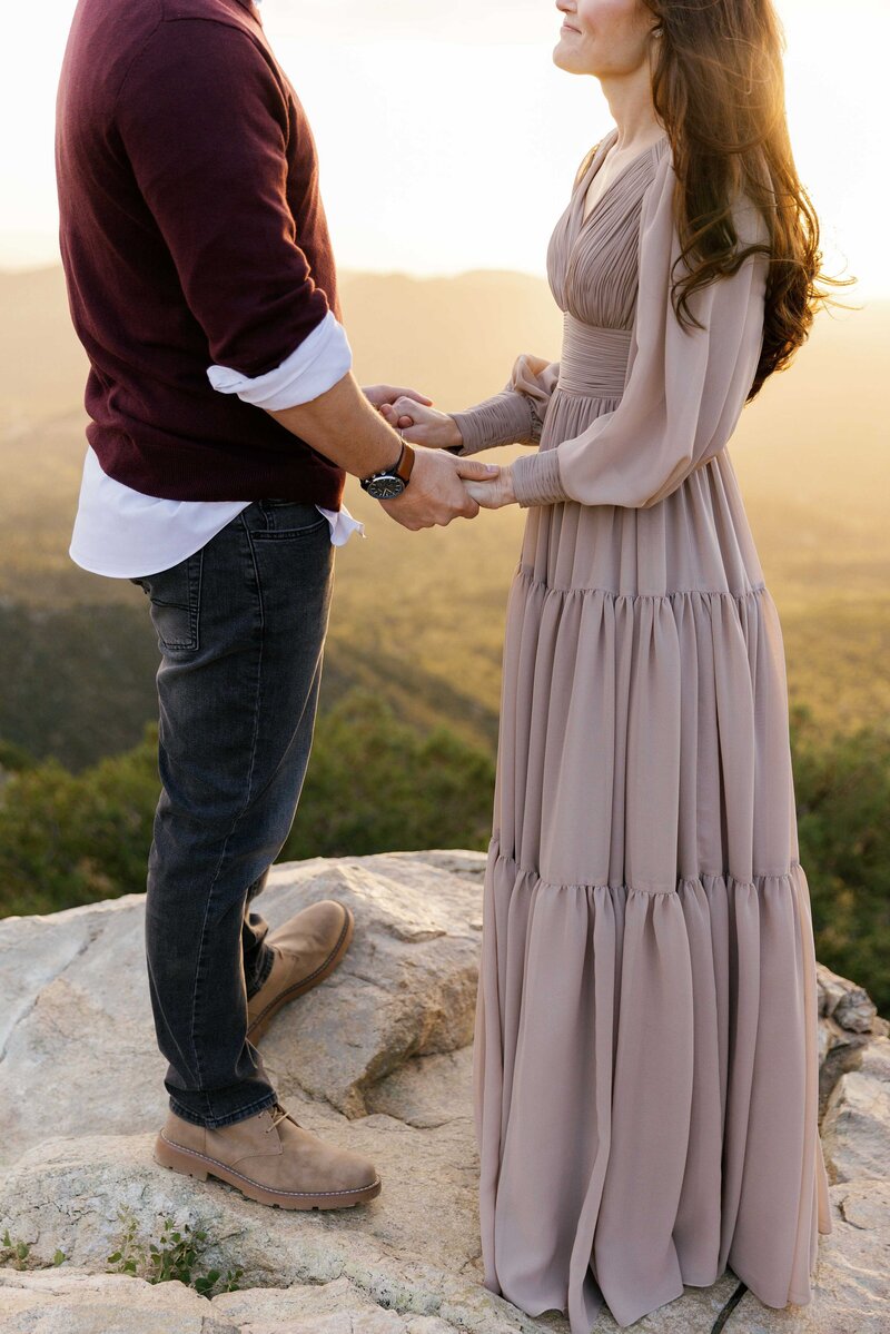 Couple stands facing each other holding hands.