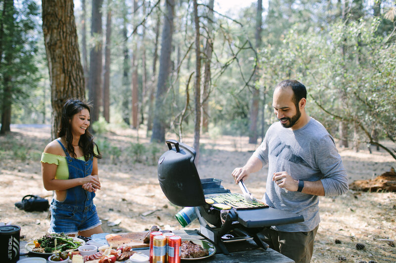 Man and woman grill together at a picnic table in a campsite