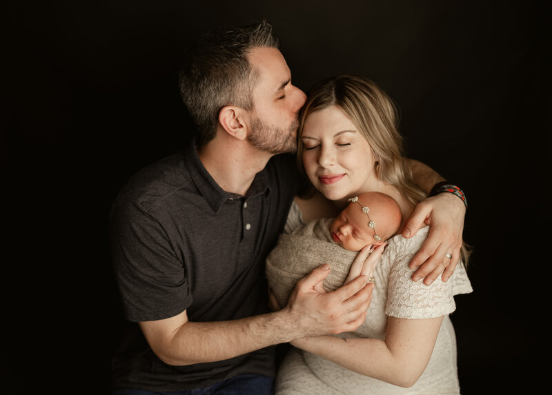 Mother holding newborn with two siblings smiling close - family newborn photography in Maple Grove Mn studio