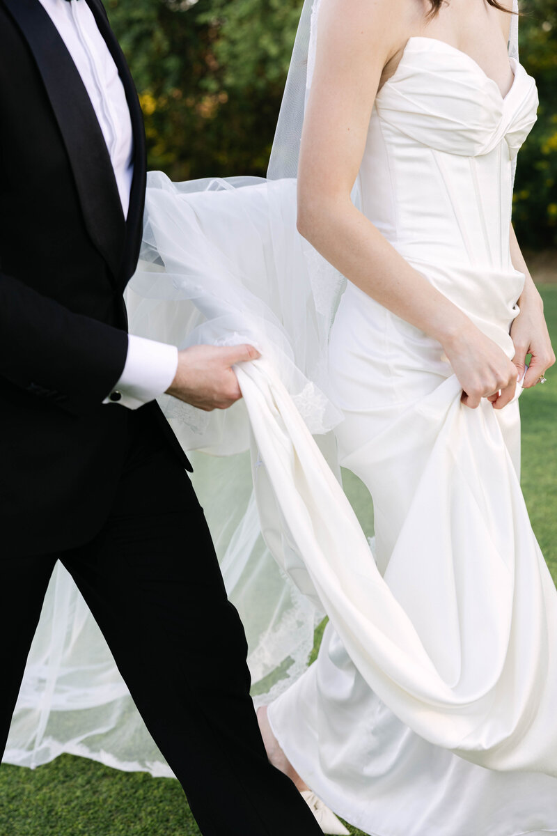 Groom holds his wife's wedding dress as they walk to their wedding reception in Scottsdale, Arizona at Paradise Valley Country Club. 