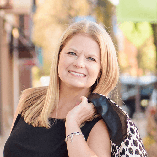 Sue Monhait wearing a black dress holding an animal print coat  over one shoulder