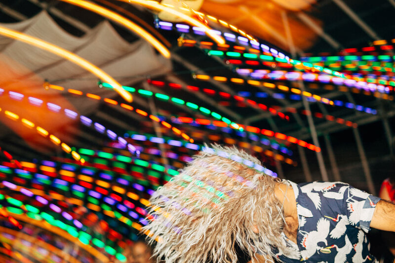 A shutter-drag emphasizes the colorful string lights as a wedding guest wearing a wig headbangs to a song in the greenhouse of Dos Pueblos Orchid Farm.