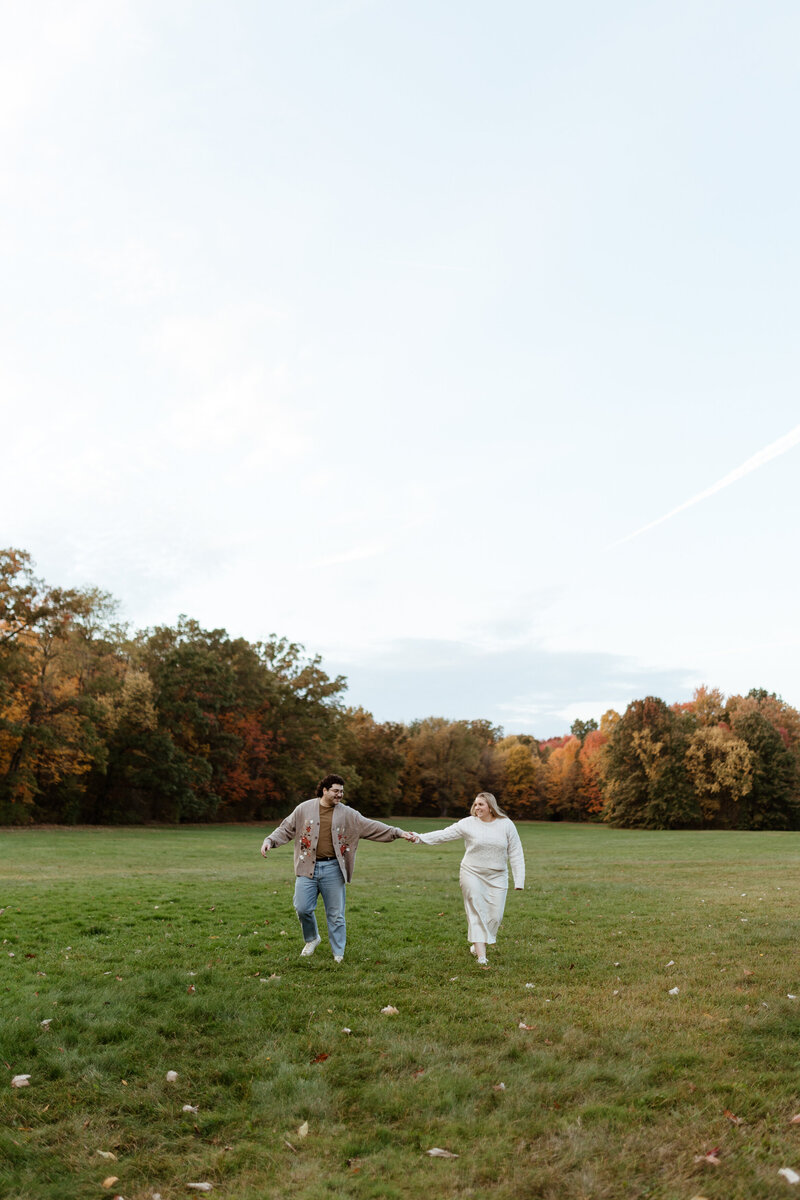 An engaged couple frolics in a field on a fall day