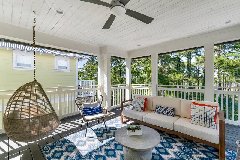 Stylish porch with cozy seating, swinging egg chair, and ceiling fan overlooking pines