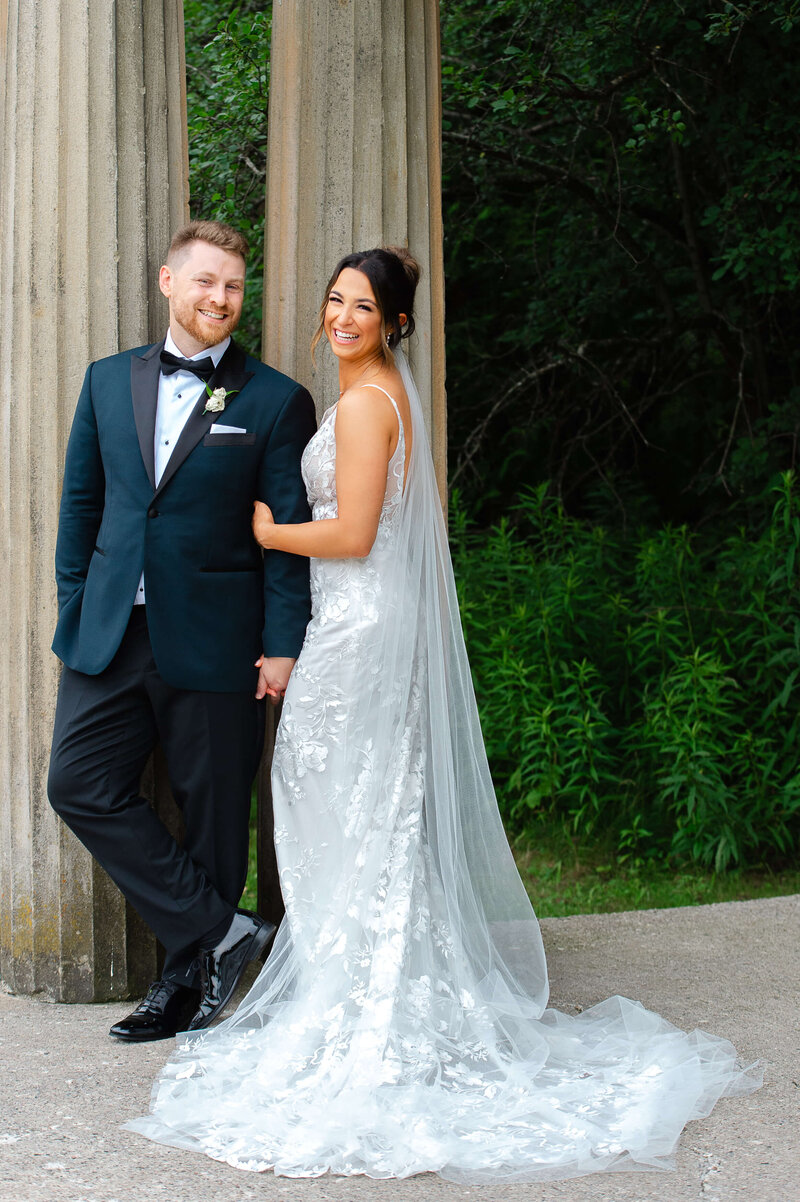 a bride with a long veil holding her groom's arm and laughing.  Taken outdoors at Eaton Hall by Ottawa wedding photographer JEMMAN Photography