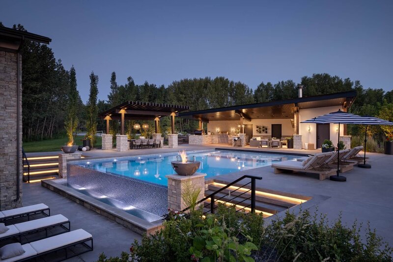 Outdoor backyard and pool with fire bowls and pergola, light features and pool loungers. 