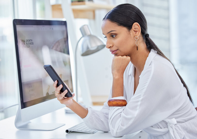 A woman holding her cellular phone sitting at an office desk.