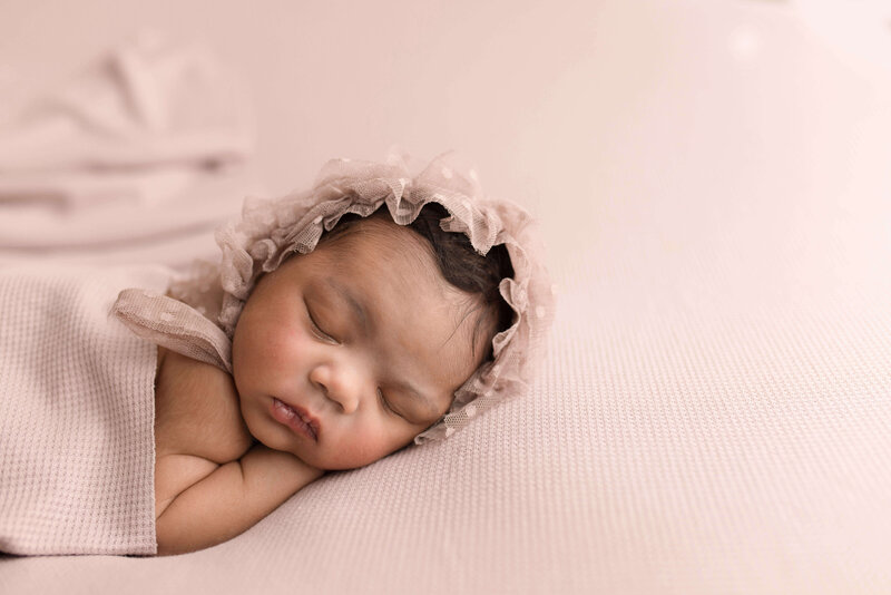 Baby girl on mauve fabric and adorable lace bonnet