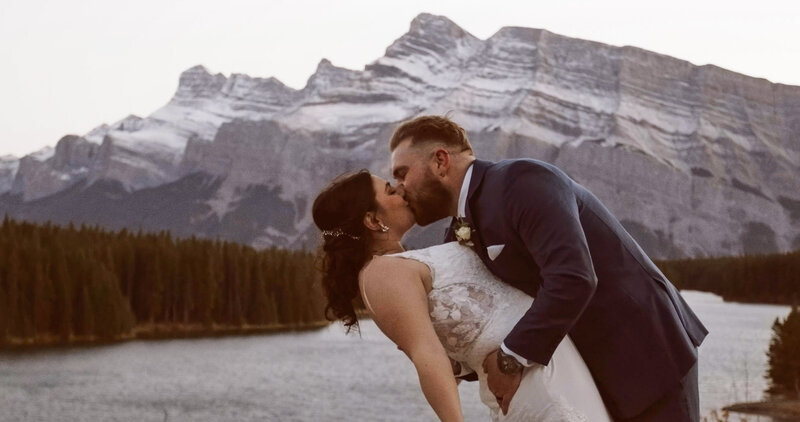 Couple sharing a kiss on a lookout above two jack lake during filming of their banff elopement video