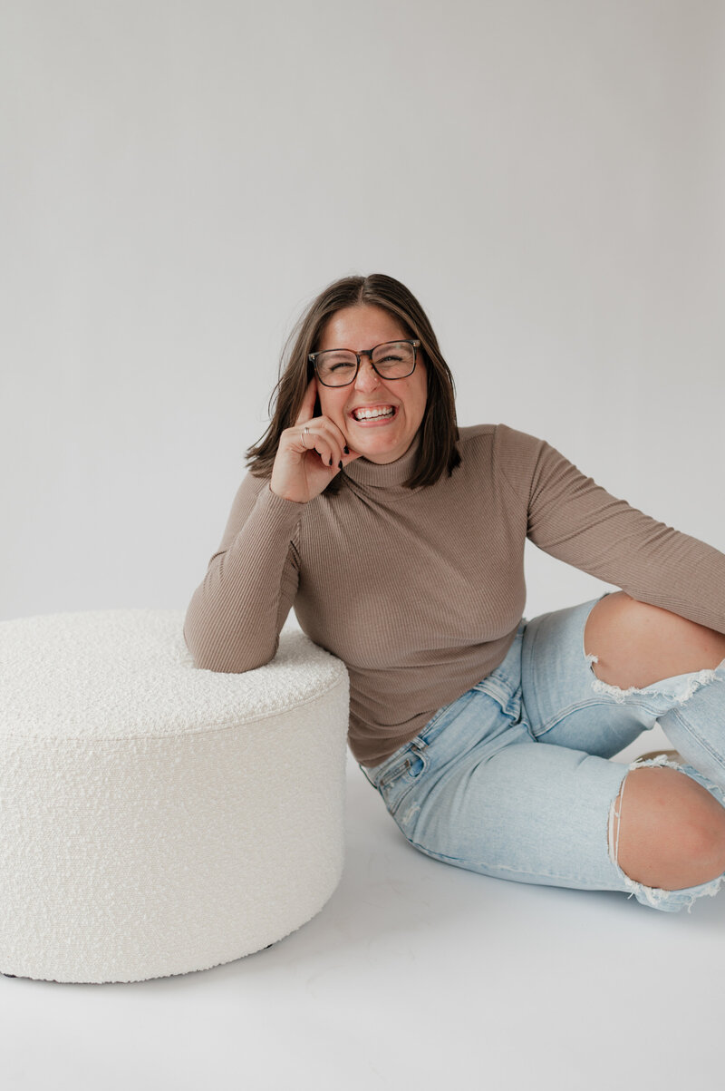 A person sitting on the ground leaning on a small ottoman and smiling 