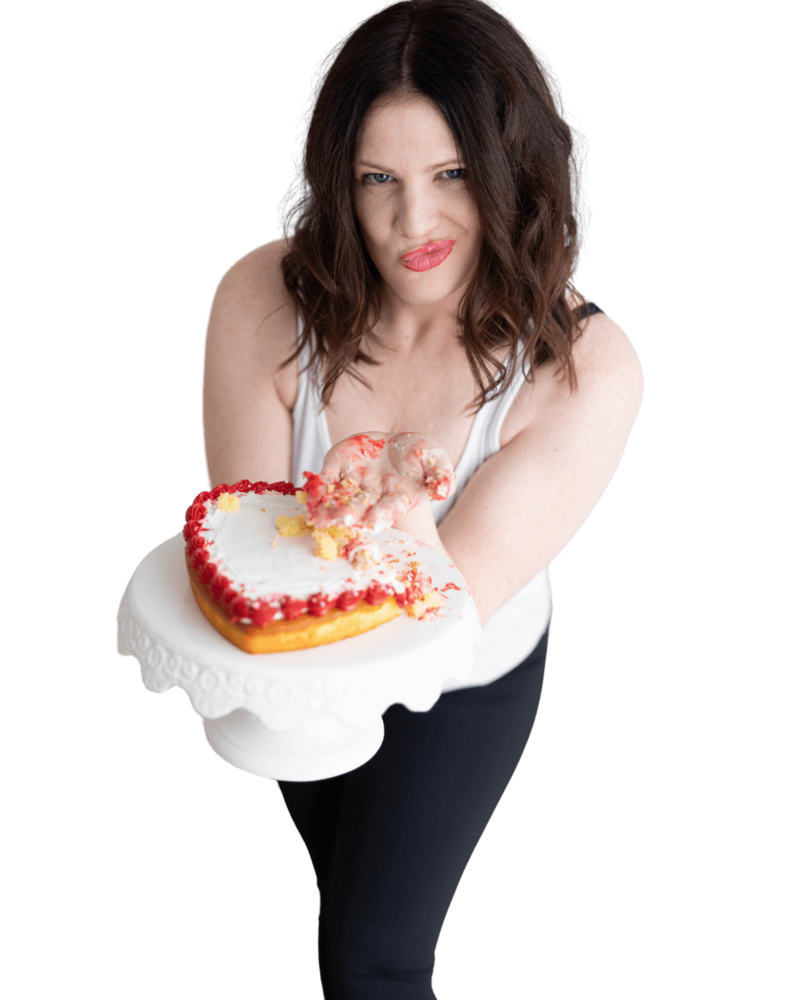 Emily, wearing a white tank top, holding a heart shaped cake with one hand smashing the icing.