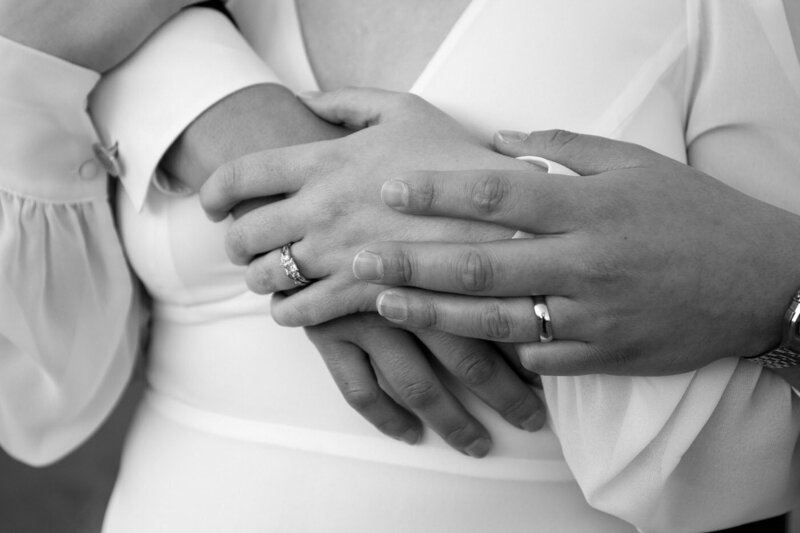 A bride holds her husband's right hand and he holds her left hand with his left hand showing off both wedding rings.
