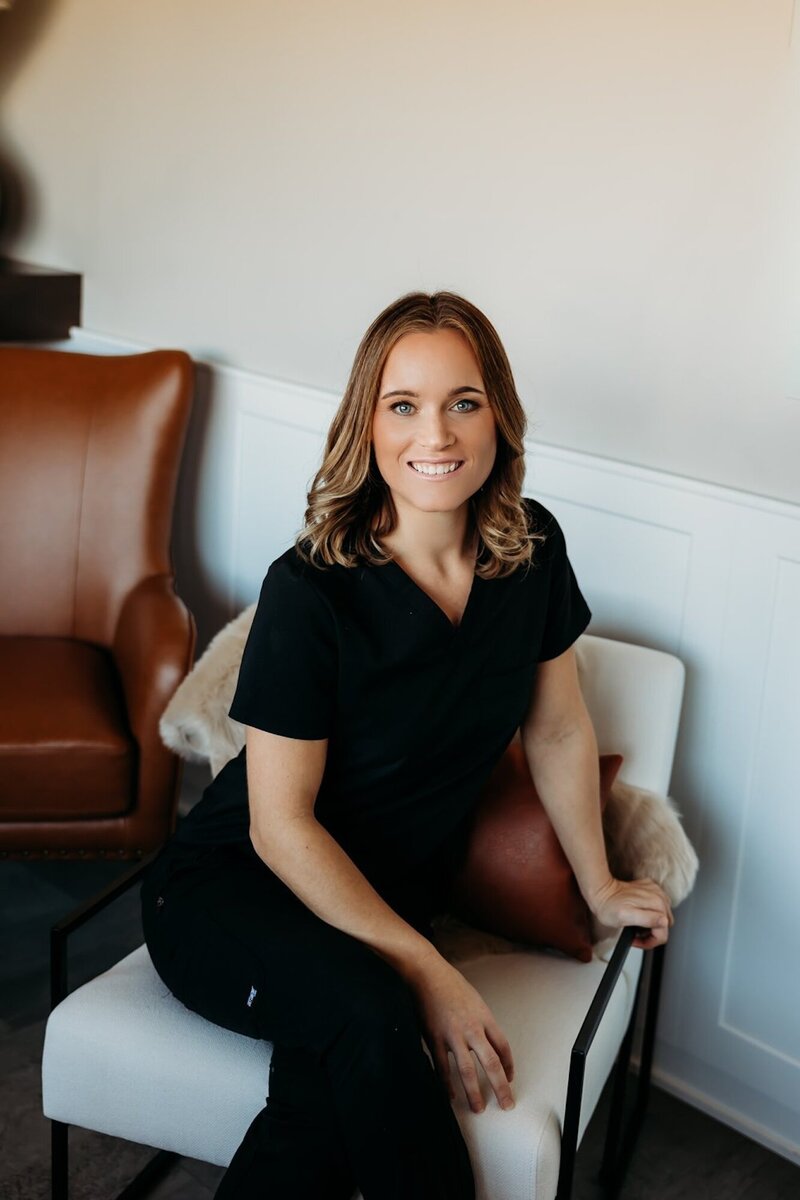 Amanda smiling, sitting in a chair at vIVid wearing black scrubs
