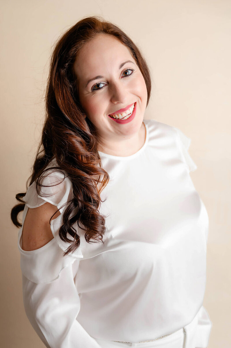 Woman in a silk long sleeve shirt, with curled hair over her right shoulder smiles happily.