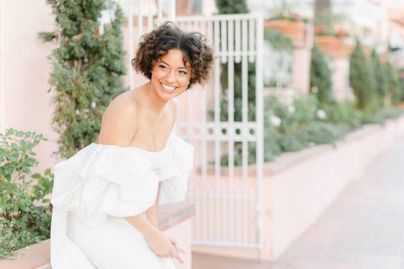 Bride smiling while sitting on the edge of planter by white gate