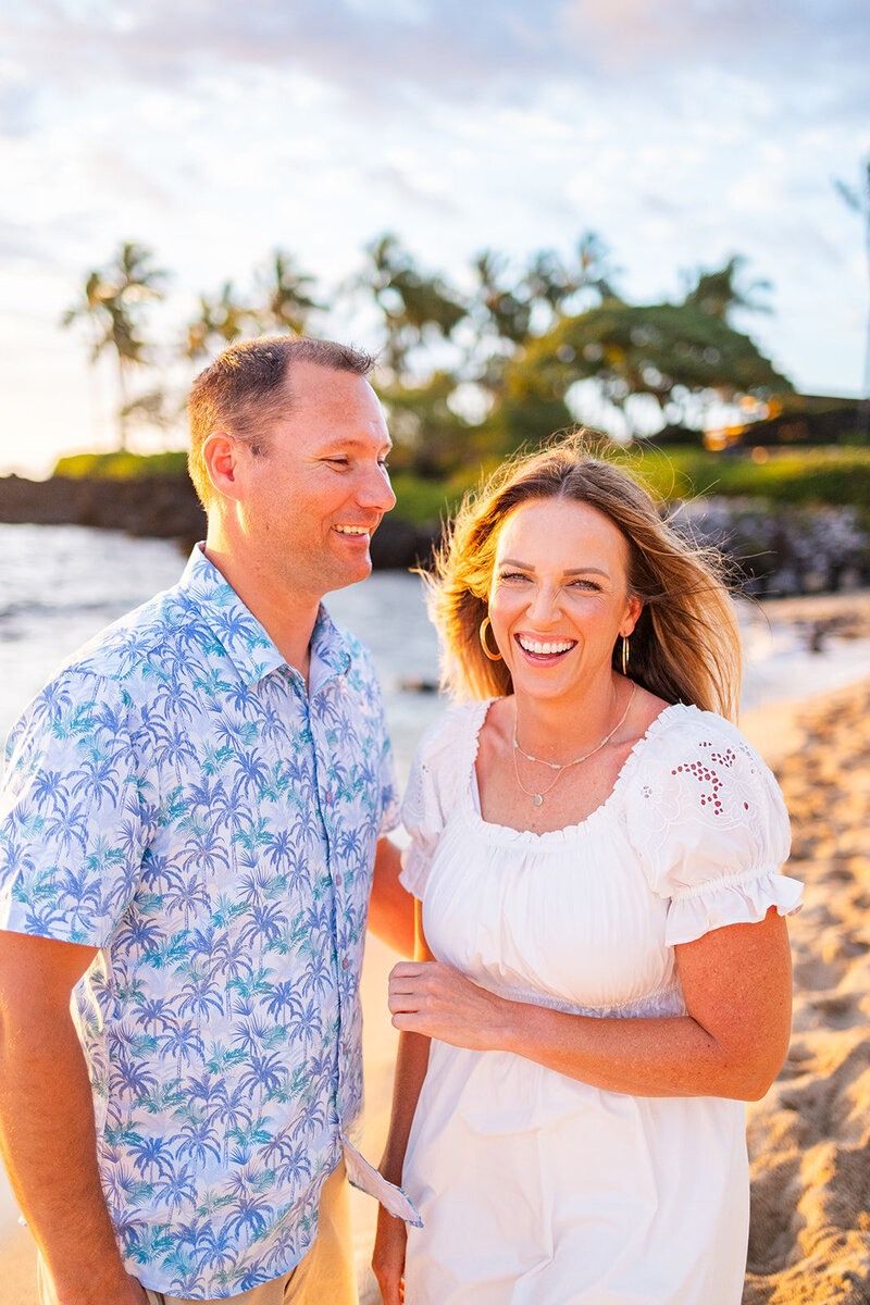 married couple laughs and woman faces camera in white dress. Palm trees and beach.
