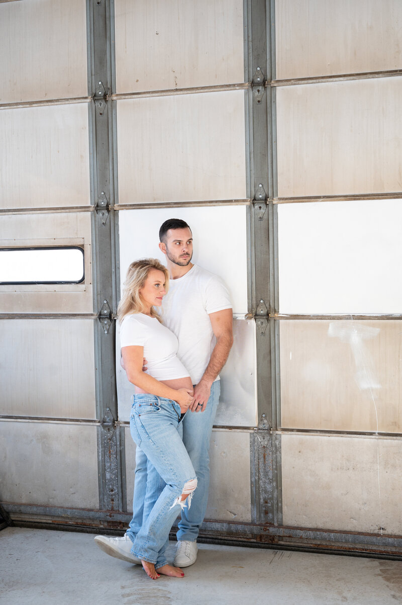 Maternity photos of couple in white shirts, jeans and industrial background