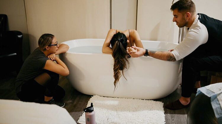 Woman in labor in a bathtub holding hands with a man