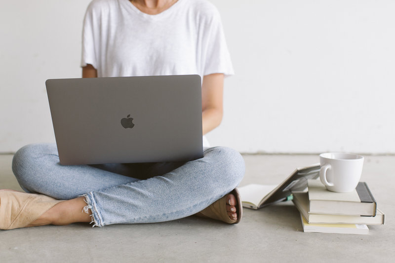 A picture of a woman sitting cross legged holding a macbook computer stock image for the Creative Bookkeeping template by Dolly DeLong Education