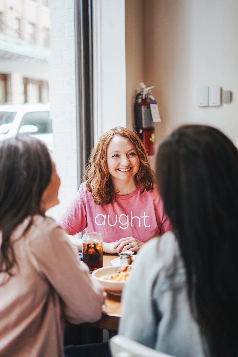 Woman in coffee shop wears pink crewneck shirt with sans-serif company logo designed by woman-owned brand agency in Knoxville, Liberty Type