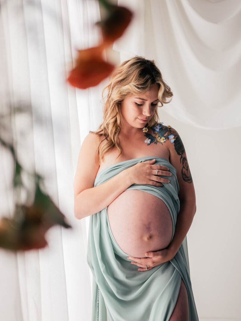 Woman shows pregnant belly while wrapped in teal fabric.