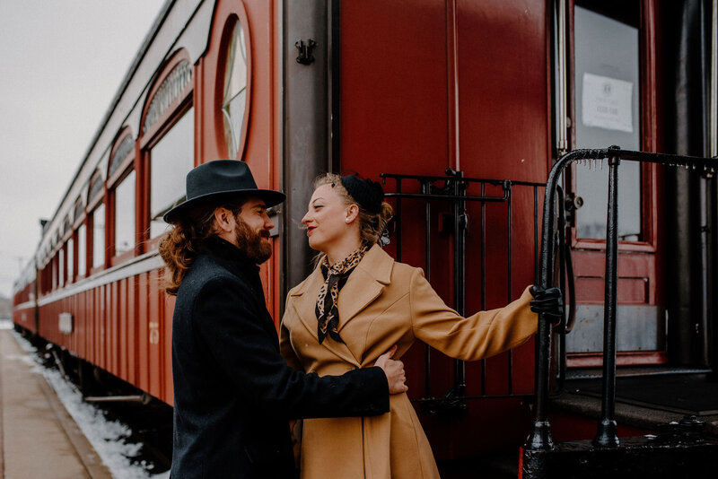 couple wearing old time vintage winter attire standing on red train car at Strasburg Rail Road