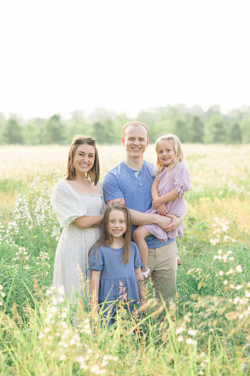 Family standing in a field of white wildflowers during their louisville family photography session with missy marshall