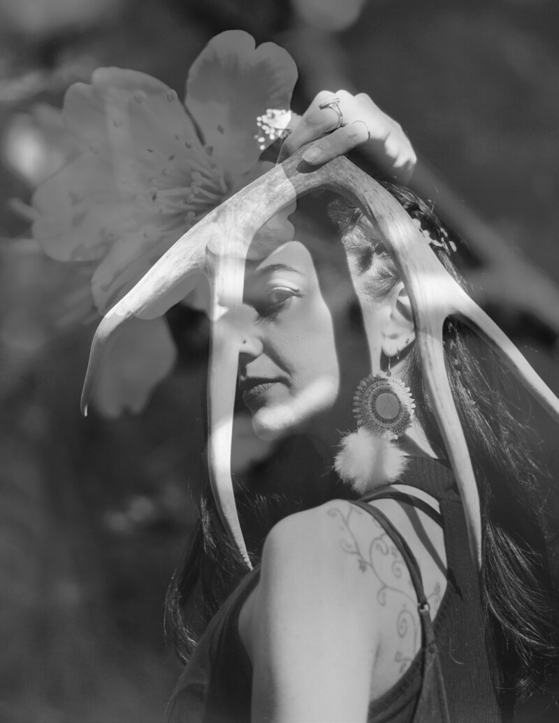 Black and white photo collage of Animal Communicator holding antler over her face overlaid with flowers.
