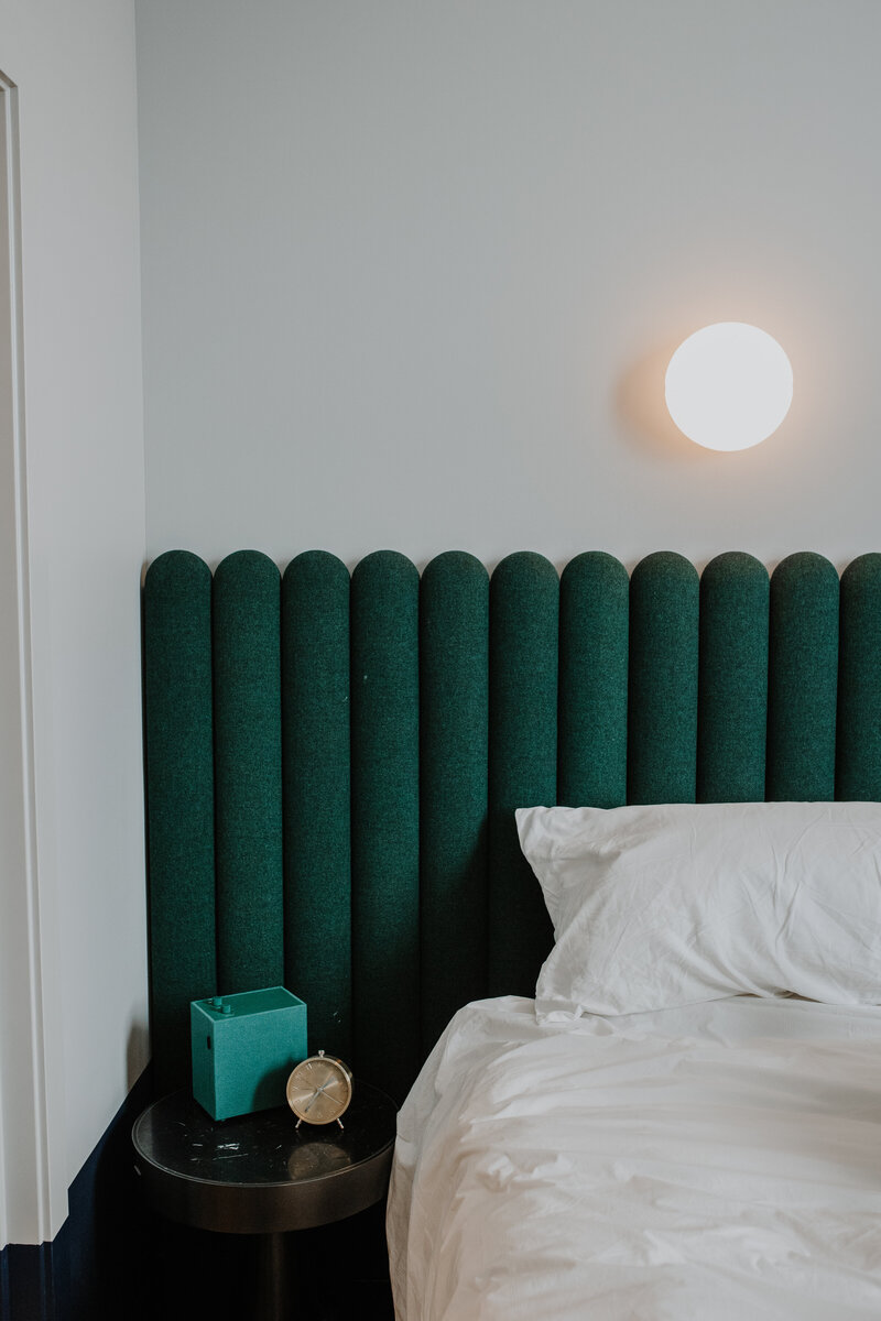 Green felt headboard behind bed with  white sheets