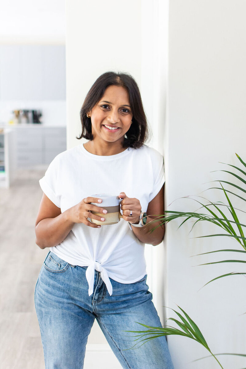 Smiling picture of a woman wearing white top and jeans  holding coffee mug