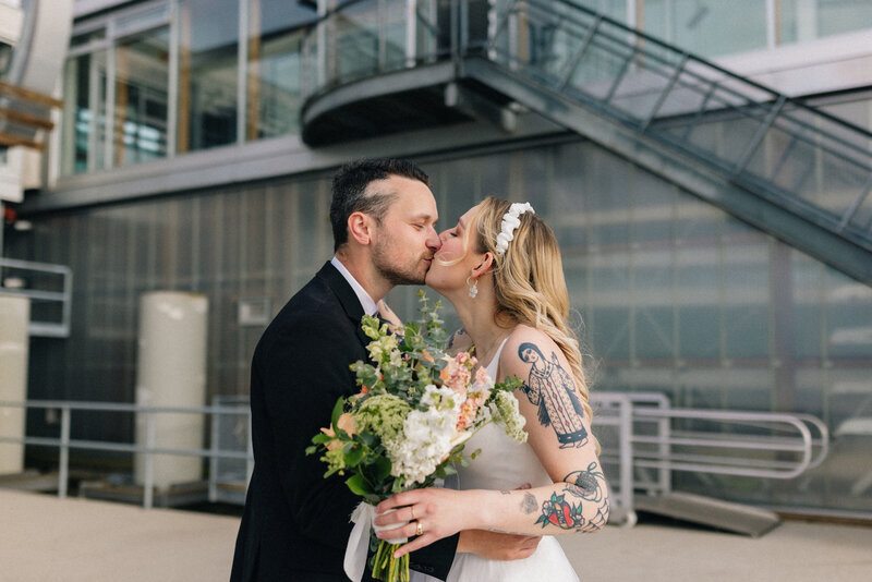 young wedding couple kissing and holding a bouquet at ubc boathouse