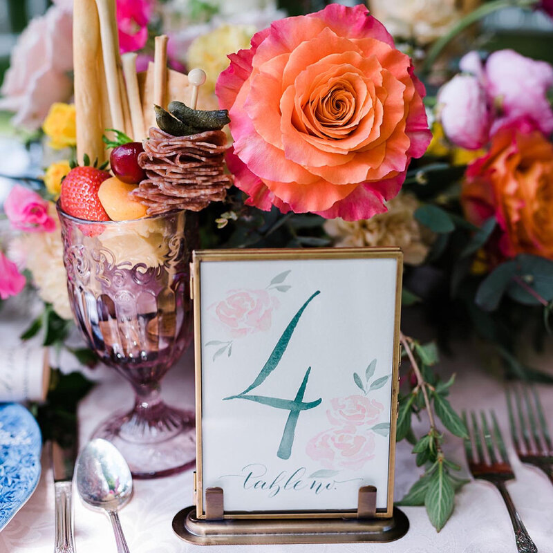 Custom table number calligraphy and the floral centerpiece behind