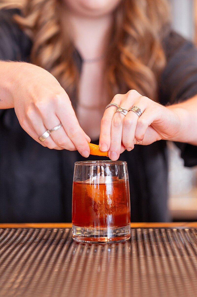 Female bartender twisting an orange over an old fashion
