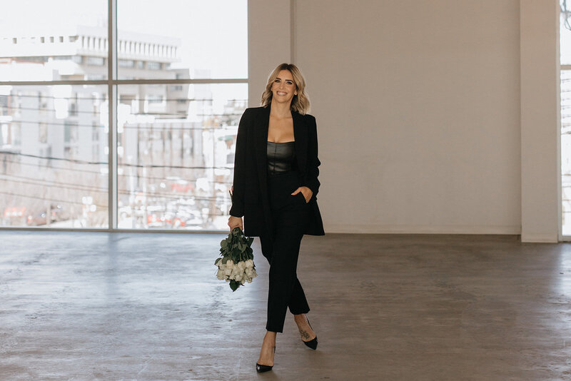 Woman holding bouquet of white roses in black suit for branding photoshoot.
