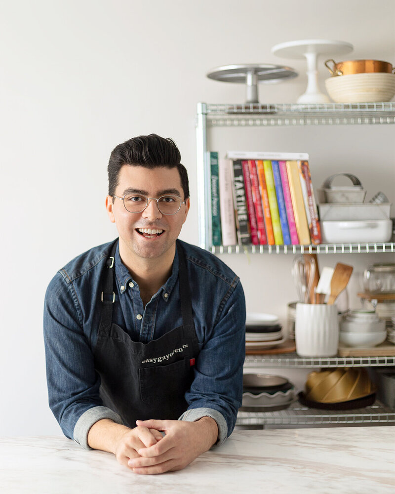 Eric King easygayoven leaning on a marble countertop in front of shelves filled with bakery items