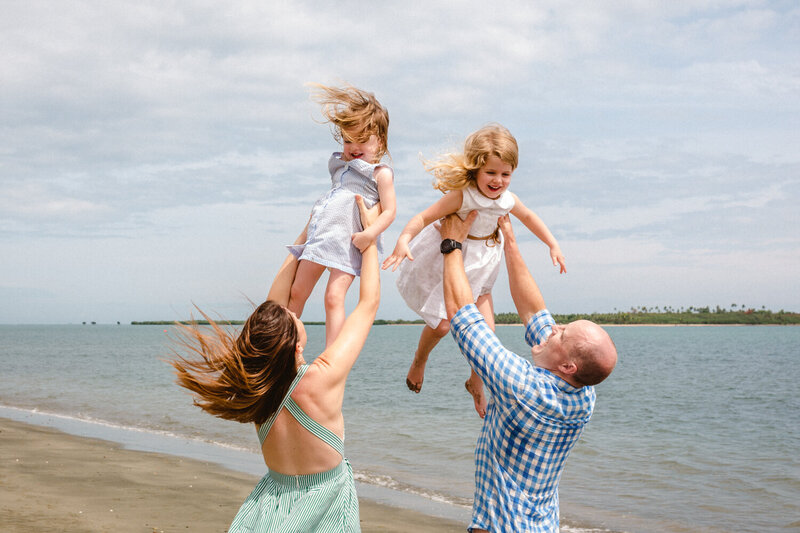 Family on the beach tossing their little girls in the air with big smiles