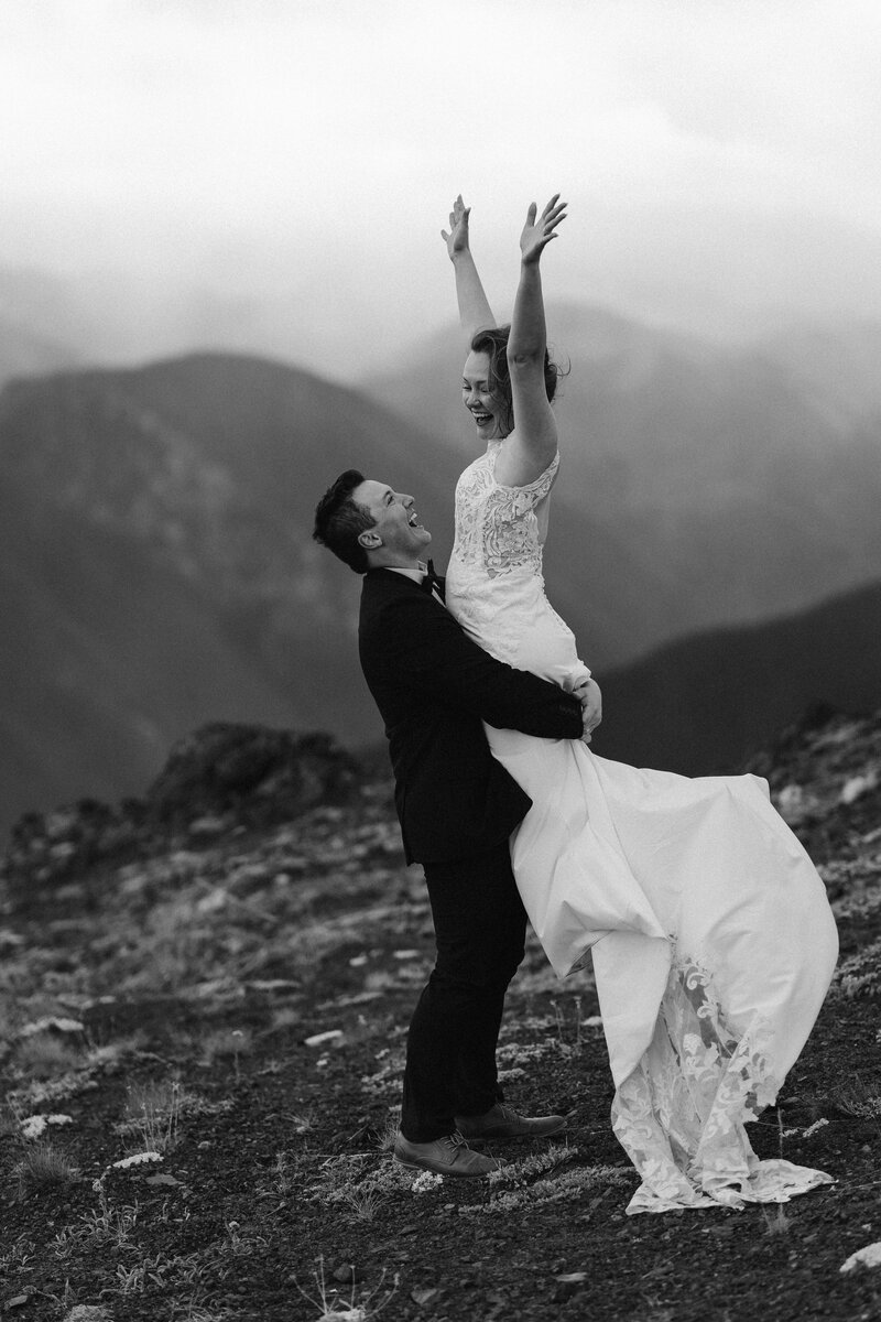 Groom picking up his bride after their elopement, with the bride in a crepe and lace gown and the groom in a suit