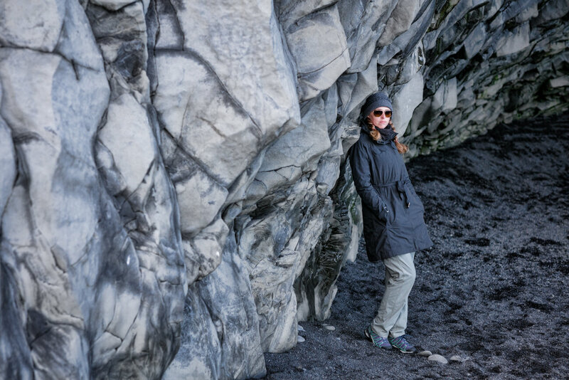 Jen Stitt standing on a stunning black sand beach in Iceland, capturing the dramatic and unique beauty of the landscape while creating unforgettable moments during an engagement session.